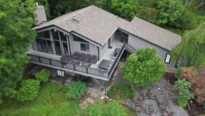 A two-story house with a balcony, large windows, and a stone pathway leading to outdoor seating. - Enjoy Cabin Vibes & Lake Views, Close to Town, Lake & FLX Activities; EV Charger (Canandaigua)