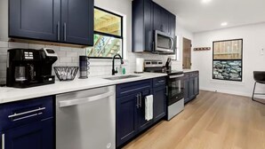 A modern kitchen with dark blue cabinets, a stainless steel dishwasher, a microwave, and a coffee maker.