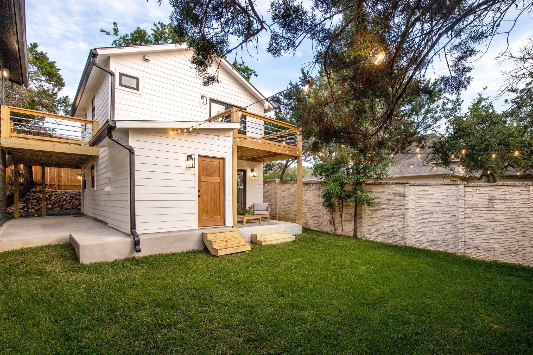 A two-story house with a wooden deck, a small porch, and a stone wall.