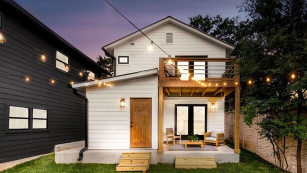 A two-story house with a balcony, string lights, and a small porch with seating.