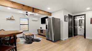 A modern kitchen with a large stainless steel refrigerator, wooden ceiling beams, and a dining area with a round table and chairs.