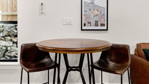 A round wooden table with two brown leather chairs, a framed picture of a building on the wall, and a stone wall in the background.