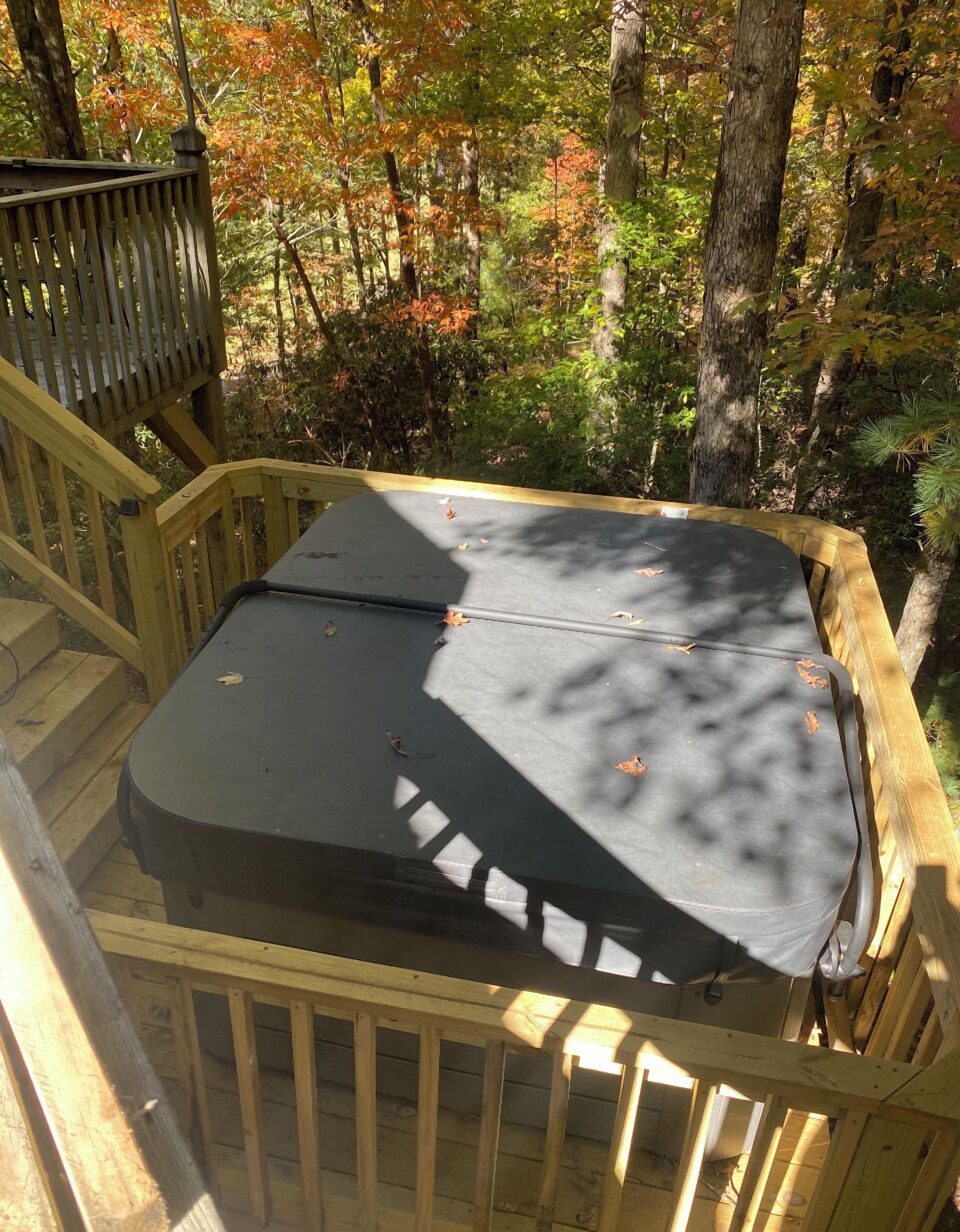 A deck with a black outdoor seating area surrounded by wooden railings, overlooking a forested area with autumn foliage.