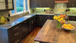 A modern kitchen with dark cabinets, a large island, and a view of the outdoors.