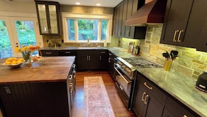 A modern kitchen with dark cabinetry, a large island, a stone backsplash, and a view of greenery outside.