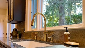 A kitchen with a large sink, a gold faucet, and a window with a view of trees.