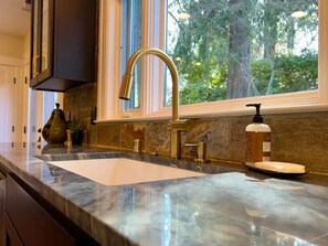 Enjoy a kitchen with a large sink, sleek faucet, and a window offering a view of the surrounding trees.