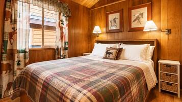 Una stanza con rivestimento in legno, un letto, due lampade a parete e una finestra con tende.
