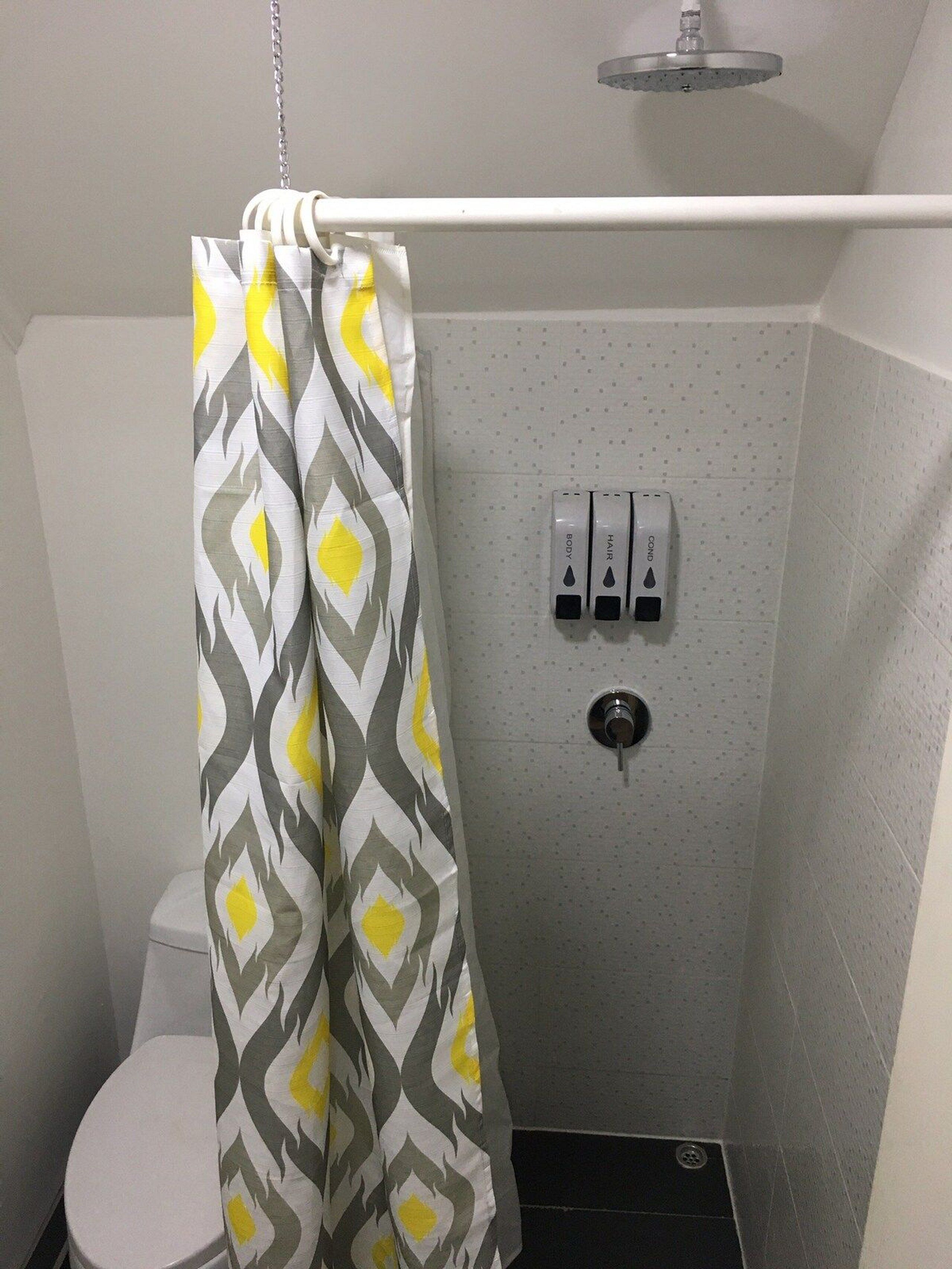 A small bathroom with a shower curtain, toilet, and hand soap dispensers.