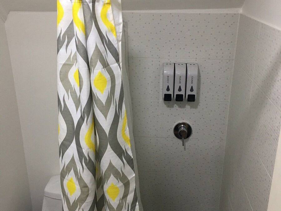 A small bathroom with a shower curtain, toilet, and hand soap dispensers.