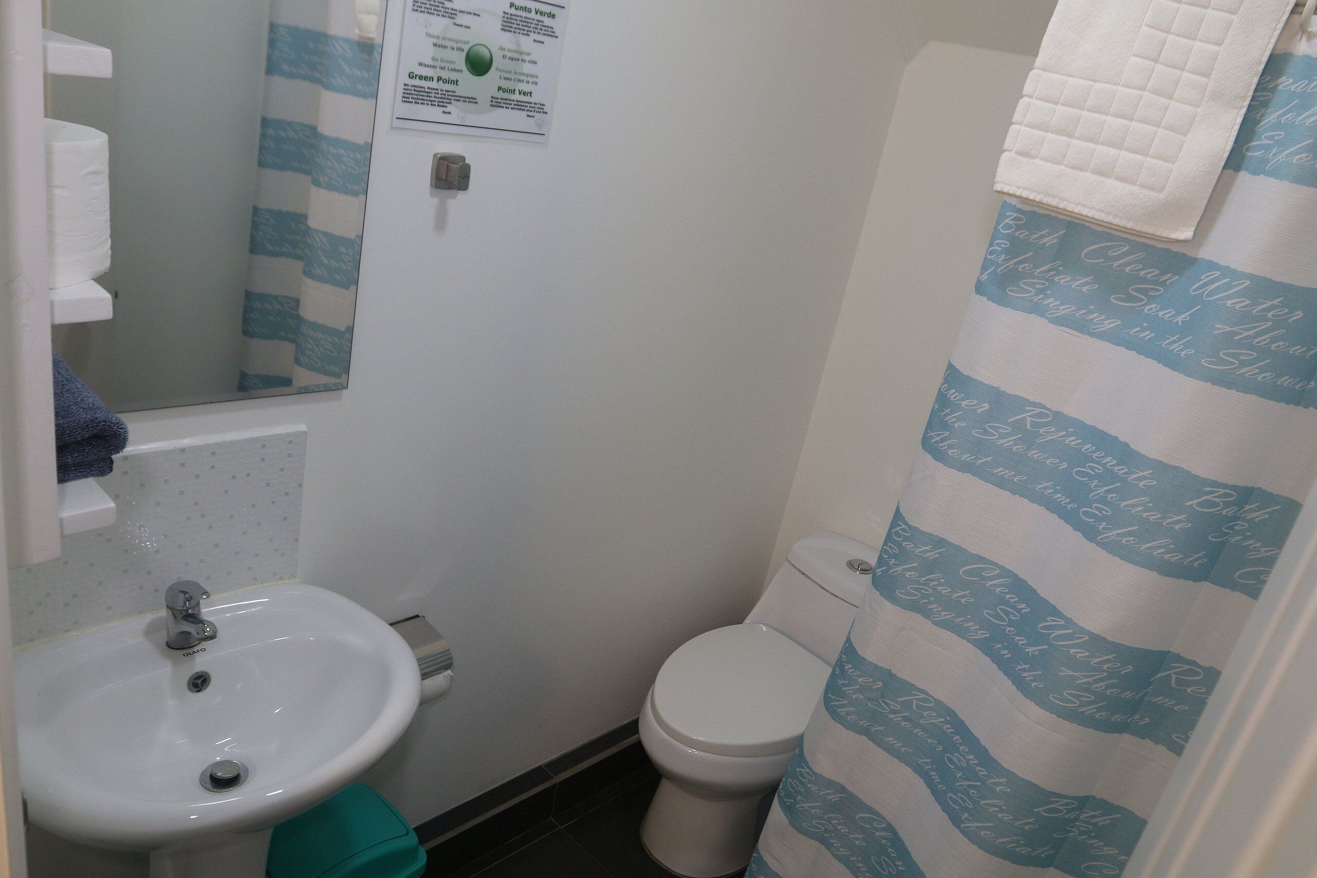 Un baño con lavamanos blanco, inodoro y cortina de ducha a rayas azules.