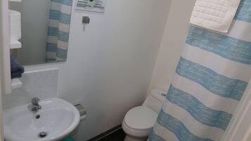 Un baño con lavamanos blanco, inodoro y cortina de ducha a rayas azules.