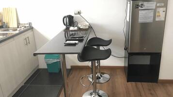 Une petite cuisine équipée avec un réfrigérateur en acier inoxydable, une machine à café et un petit tabouret de bar.