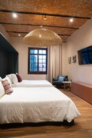 A bedroom with a large bed, a chair, a small table, and a window with curtains.