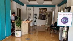 A hotel reception area with a receptionist, a sanitation point sign, and a potted plant. - Hotel Punto Poza Rica (Poza Rica)