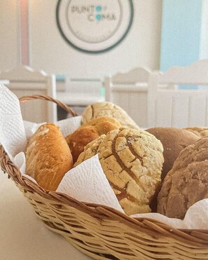 A basket of assorted breads on a table with a white fence and a sign in the background.