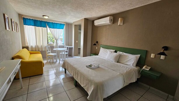 A hotel room with a bed, a desk, a yellow chair, a small table, and a window with curtains. - Hotel Punto Poza Rica (Poza Rica)