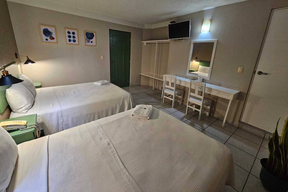 A hotel room with two beds, a desk, a chair, a television, and a green door.