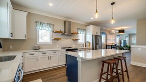 Une cuisine moderne avec des meubles blancs, un grand îlot central doté de tabourets et un éclairage suspendu.