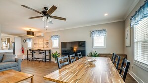 Un salon spacieux avec une grande table à manger en bois, des sièges confortables, un ventilateur de plafond et un téléviseur.