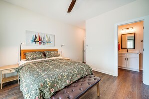 Een slaapkamer met een bed, een bankje, een nachtkastje, een schilderij en een zichtbare badkamer door een open deur.