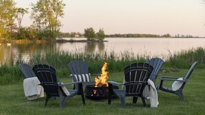 Ein Seeufer mit vier Adirondack-Stühlen, die um eine Feuerstelle angeordnet sind.