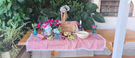 A table set outdoors with a checkered tablecloth, various fruits, flowers, and a bottle.