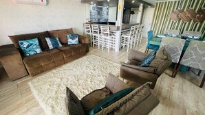 Un salon avec un ensemble de canapés marron, un tapis blanc et un coin repas avec un mur à rayures et un bar.