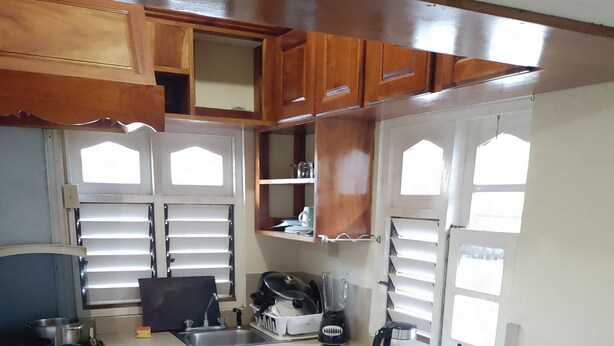 A compact kitchen with wooden cabinets, a stove, a refrigerator, and a window with blinds.