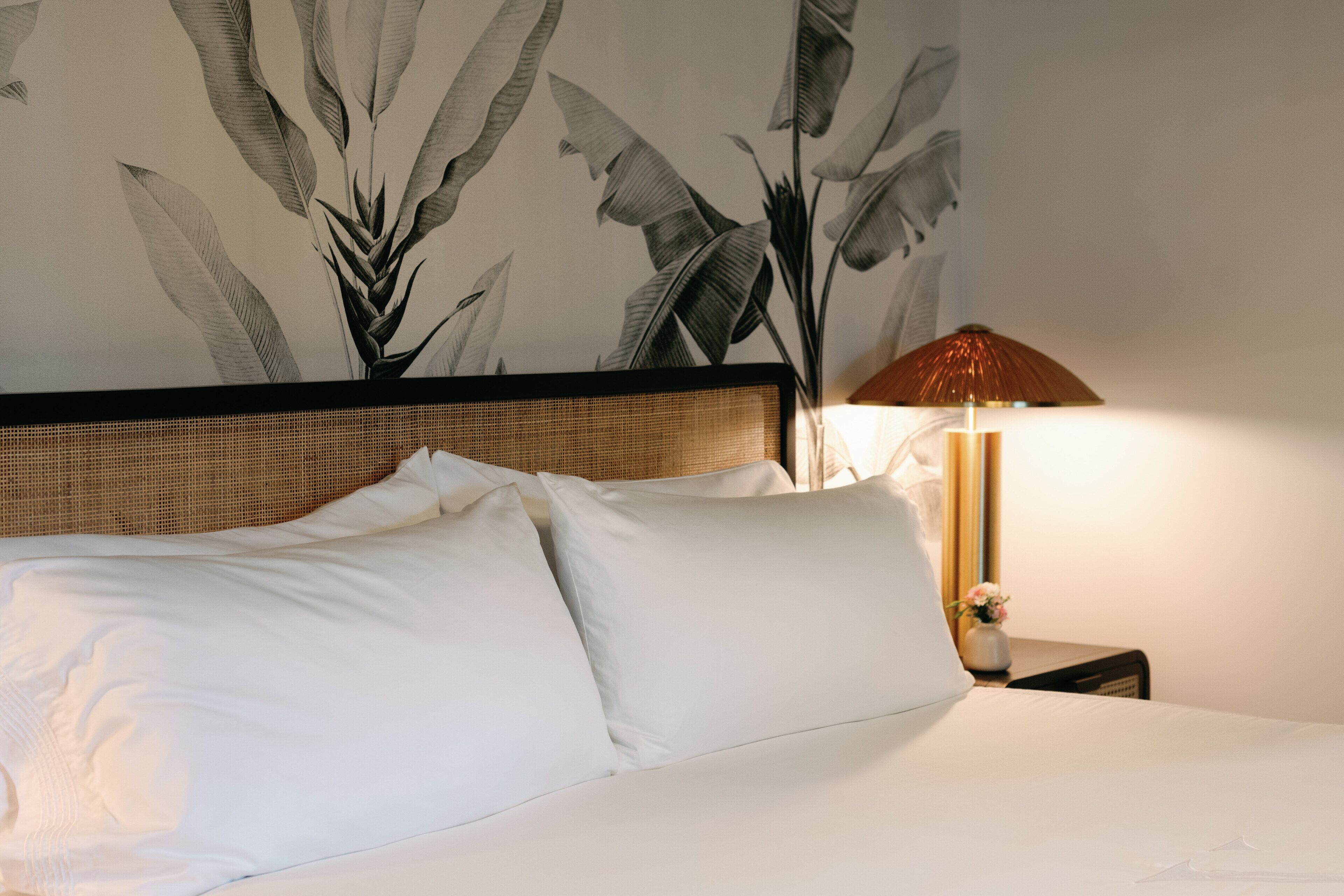 A neatly made bed with white linens and a headboard with a woven texture.