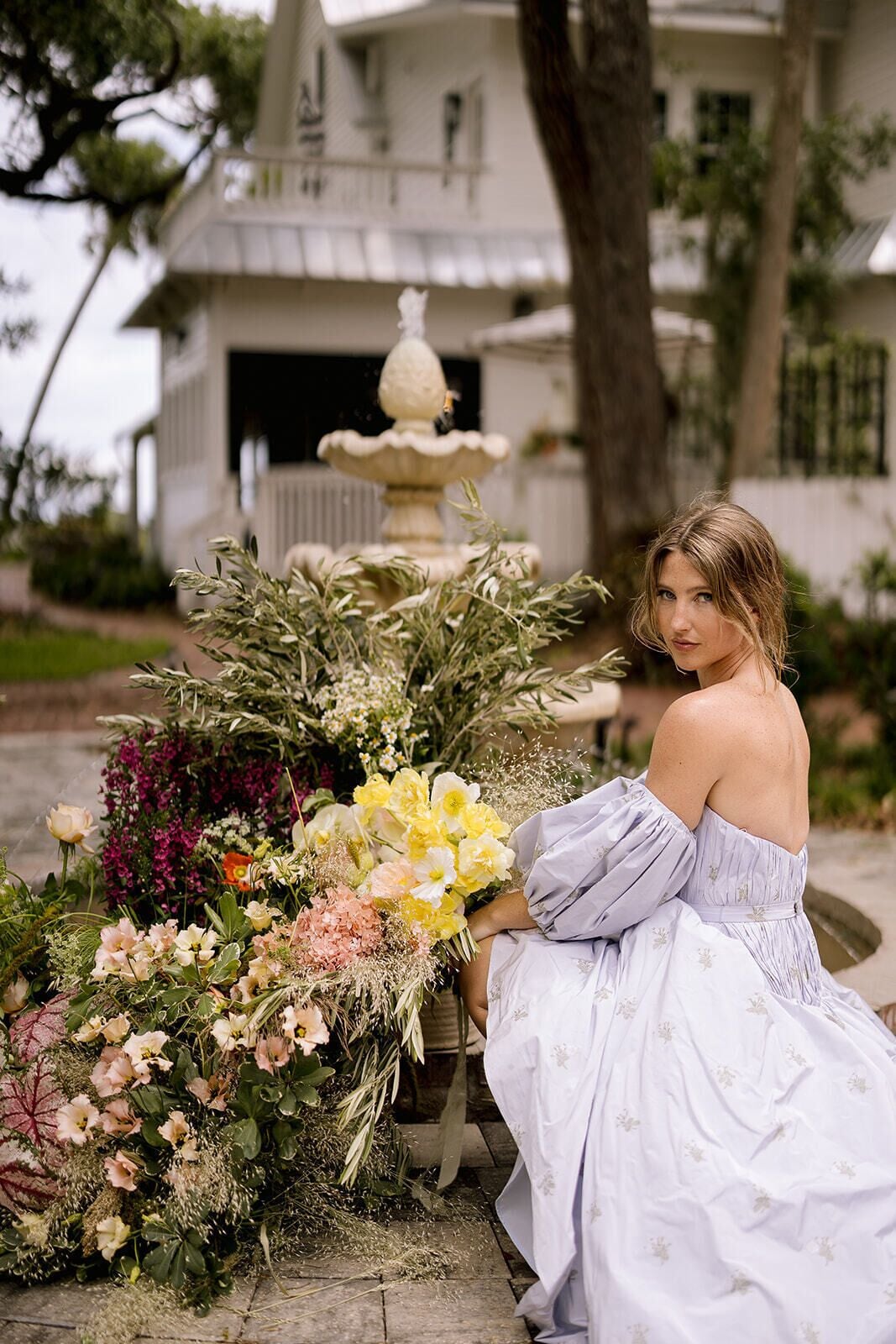 Una mujer sentada junto a una fuente con un arreglo floral.