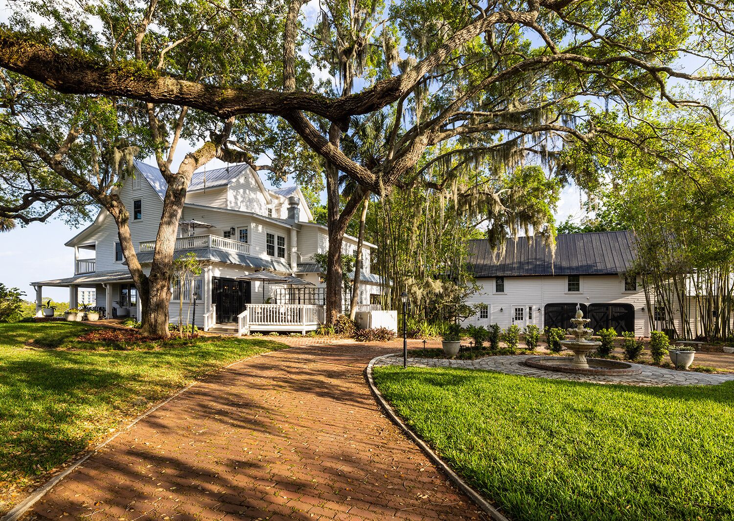 A large white house with a covered porch and a garden with a fountain.