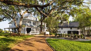 A large white house with a covered porch and a garden with a fountain.
