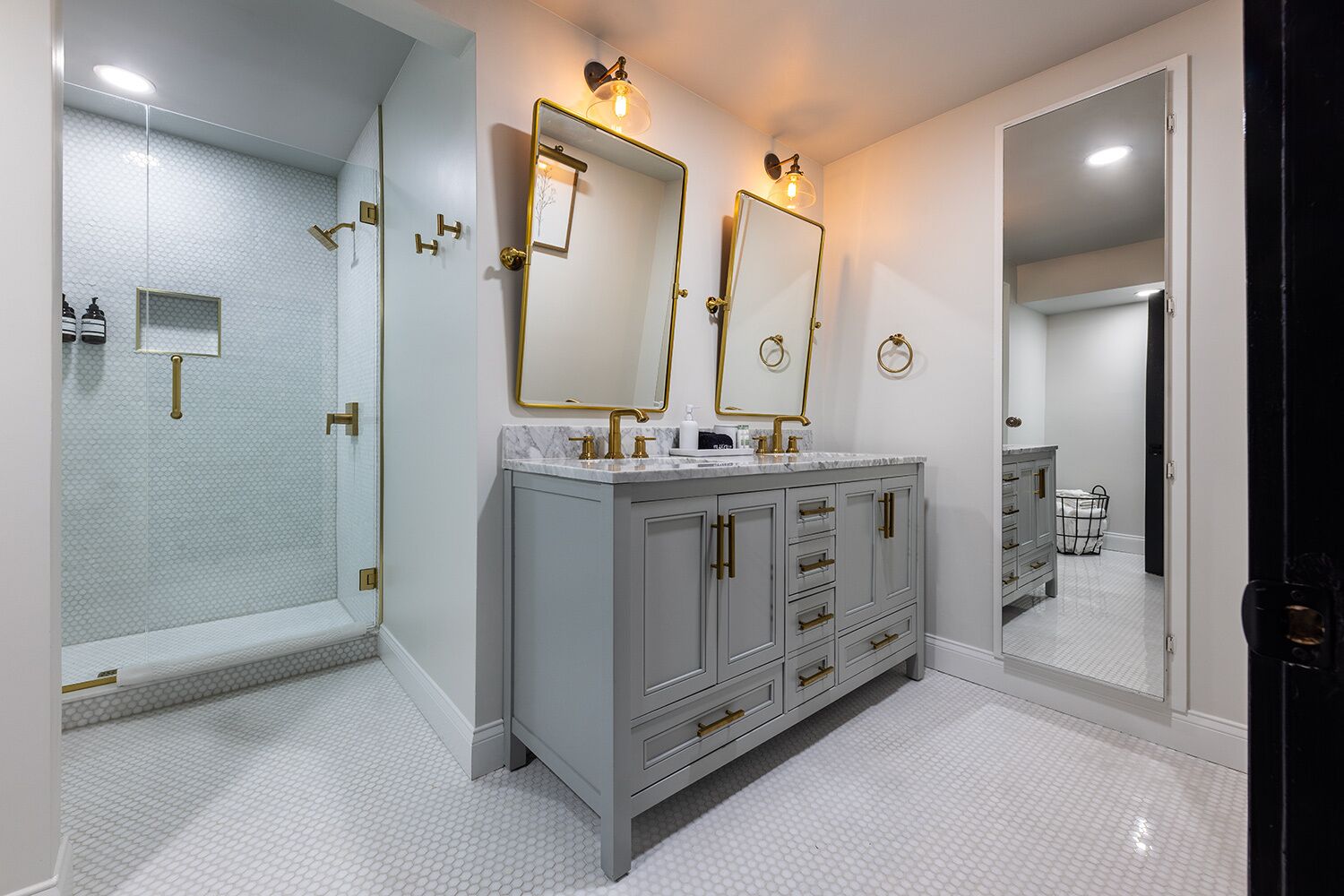 Ein modernes Badezimmer mit begehbarer Dusche, einem Waschtisch mit zwei Spiegeln und einem großen Spiegel über dem Waschtisch.