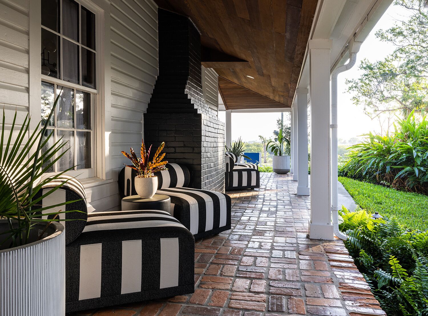 A covered outdoor seating area with black and white striped sofas and planters.