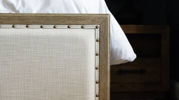 Ein Bett mit Holzgestell und Stoffpolster, ein Nachttisch aus Holz mit Lampe sowie ein Teppich mit Muster.
