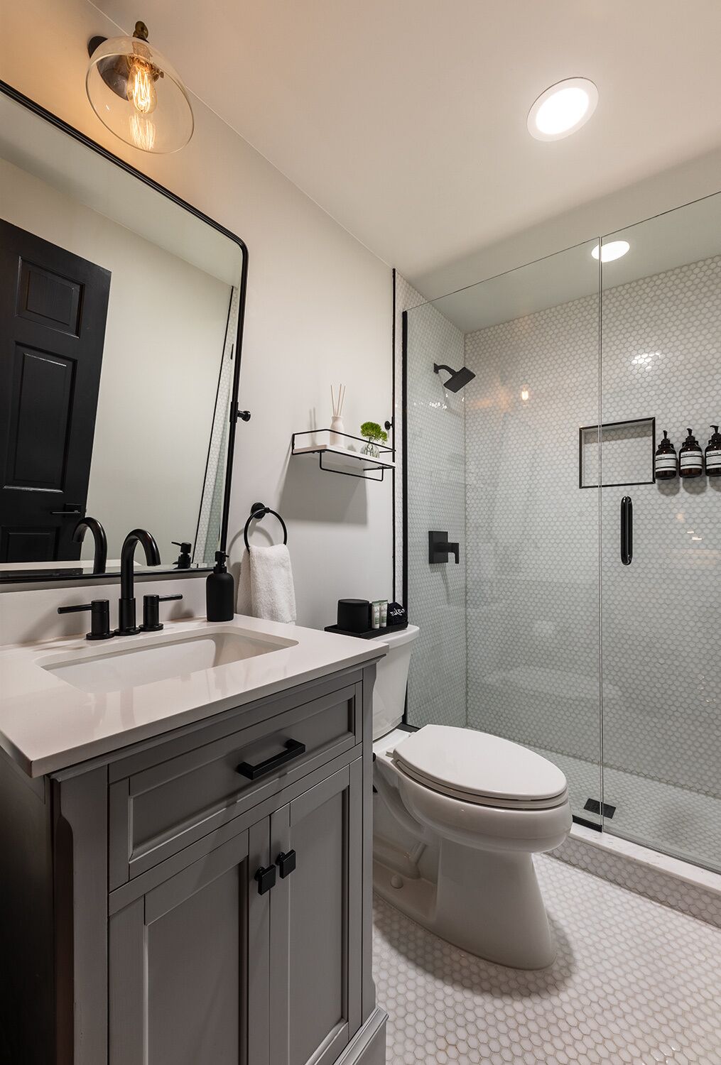 A modern bathroom with a white sink, a large mirror, a toilet, and a glass-enclosed shower area.