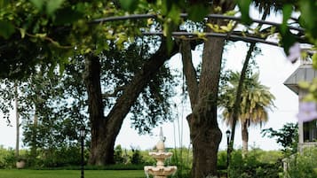 Um jardim com uma fonte central, rodeado por árvores e plantas em vasos.