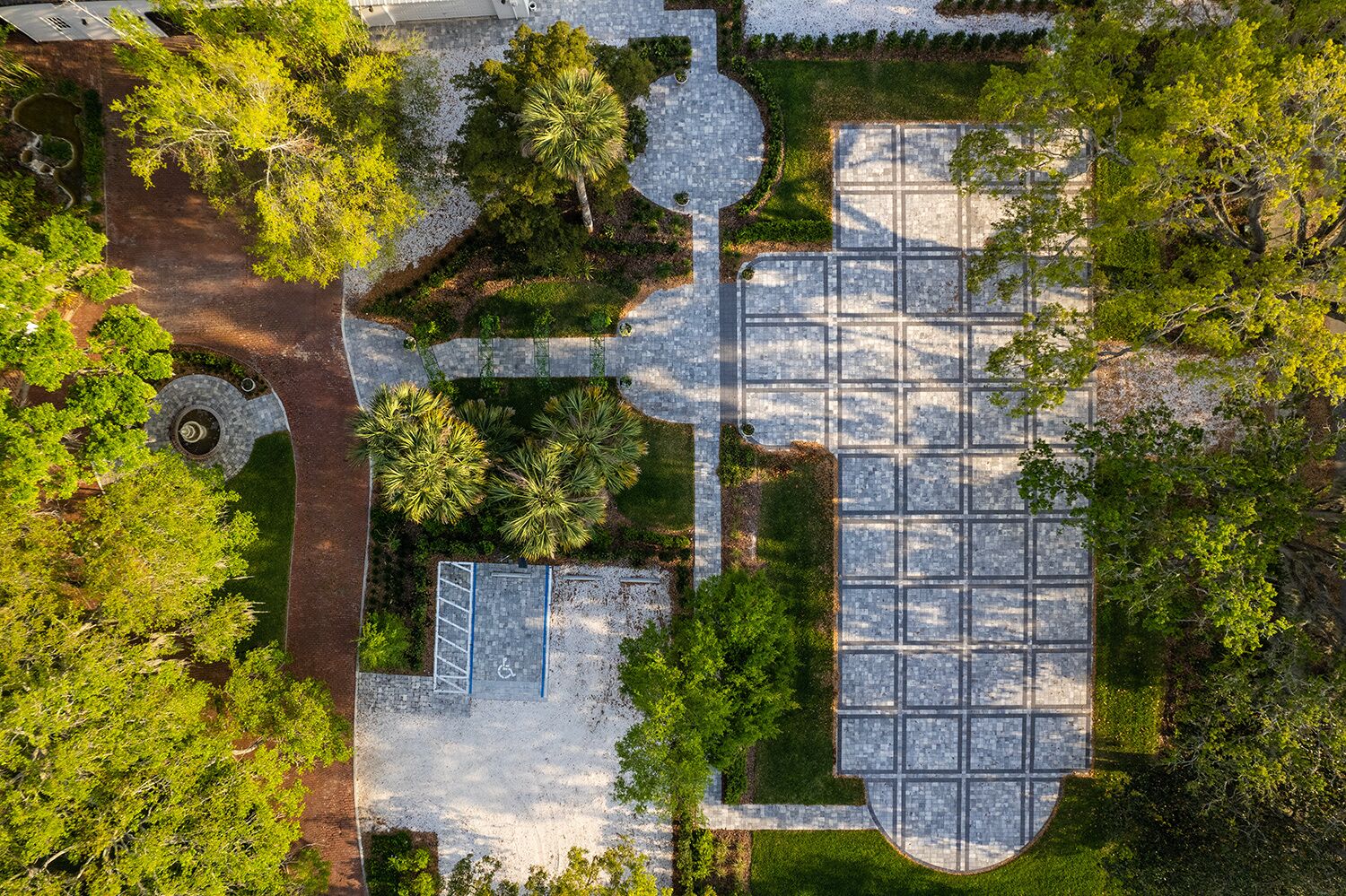 An aerial view of a landscaped area with a paved courtyard, surrounded by trees and a circular garden feature.