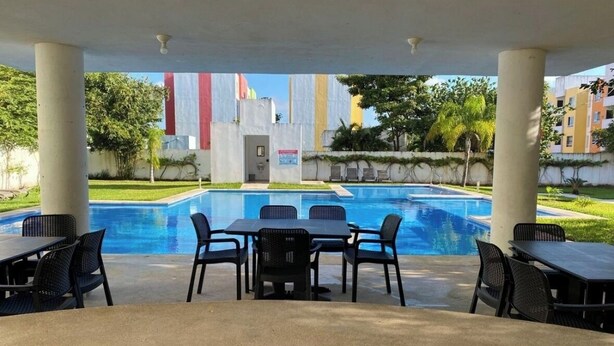 An outdoor pool area with a covered seating area, tables, and chairs. - 13 minutes away from quinta avenida (Q.R.)
