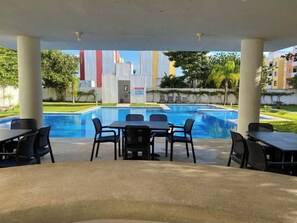 An outdoor pool area with a covered seating area, tables, and chairs. - 13 minutes away from quinta avenida (Q.R.)