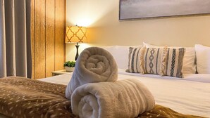 A neatly made bed with rolled towels, a patterned pillow, and a lamp on a bedside table. - Bellwood Cabin (Forest Lakes Estates)