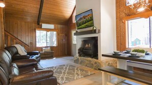 A cozy cabin interior with a stone fireplace, leather sofa, and a dining table with bowls and a plant. - Bellwood Cabin (Forest Lakes Estates)