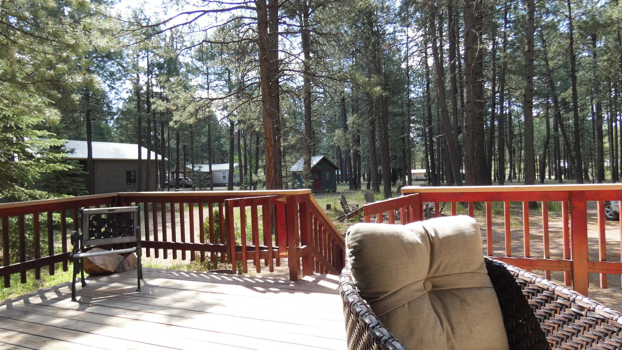 A wooden deck with a chair and a table, surrounded by tall trees.
