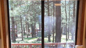 A kitchen with a double sink, a window with a view of a forest, and various toiletries on the counter. - Bellwood Cabin (Forest Lakes Estates)