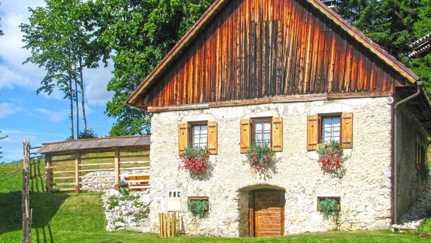 Un edificio rustico in pietra con persiane di legno, una porta in legno e fioriere.