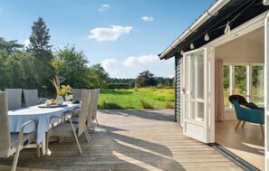 An outdoor dining area with wicker chairs and a table set for two, overlooking a grassy field and trees. - Cozy home in Gørlev with kitchen (Gørlev)