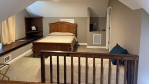 A bedroom with a wooden bed, a small shelf, a door, and a window with curtains.