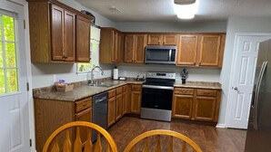 A kitchen with wooden cabinets, a microwave, an oven, and a dishwasher. There is a dining table with chairs.