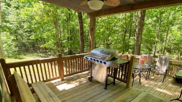 A wooden deck with a grill and a table, surrounded by trees.